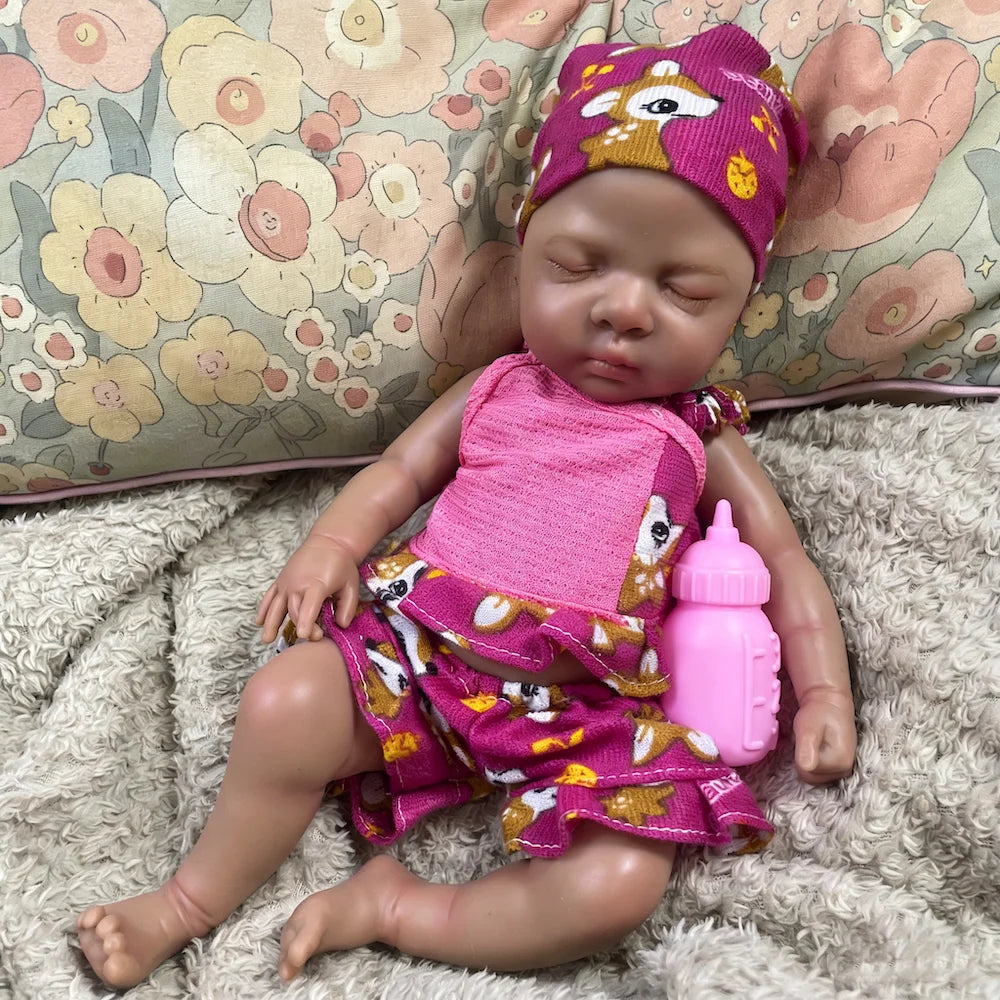 Nia, a 13-inch sleeping full silicone reborn baby girl with dark skin, in a pink print romper and hat
