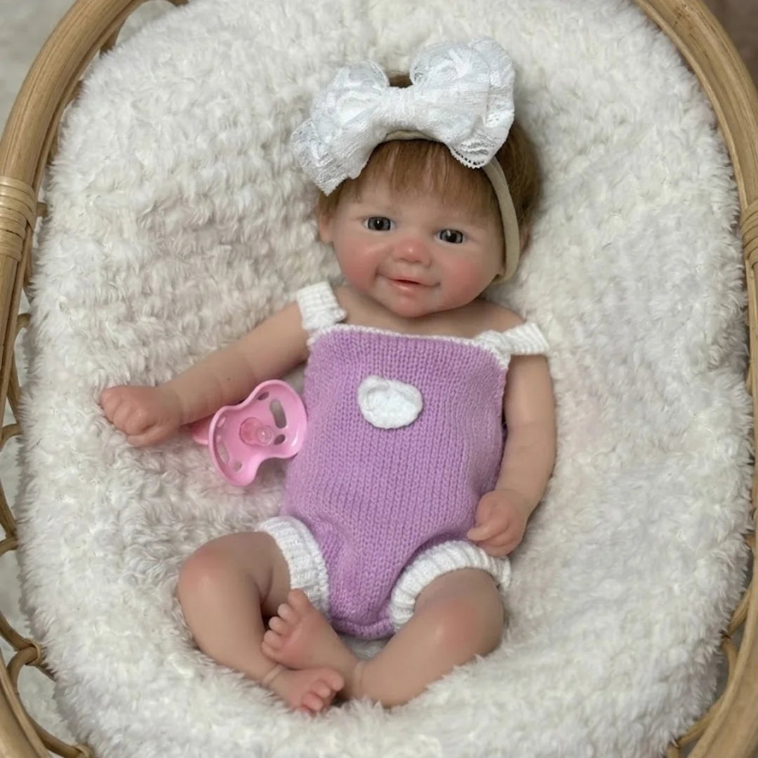 Lottie, a 13 inch solid silicone reborn baby girl with rooted brown hair, smiling in a lilac knit romper