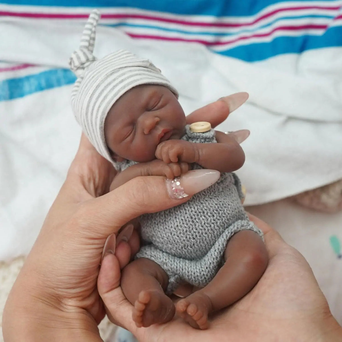 Miles sleeping in a gray knit romper and striped hat, cradled in a hand
