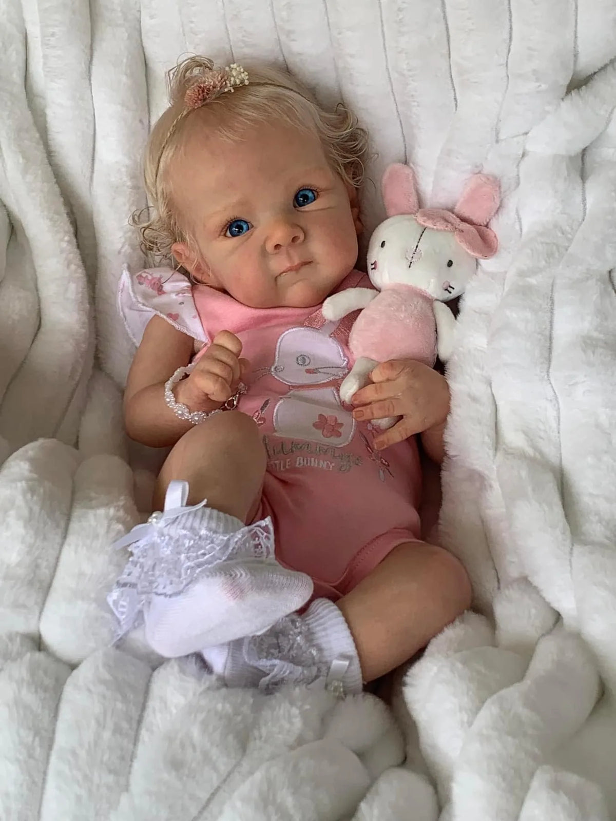 Sadie, an 18-inch awake reborn baby girl with blonde rooted curls and blue eyes, in a pink bodysuit